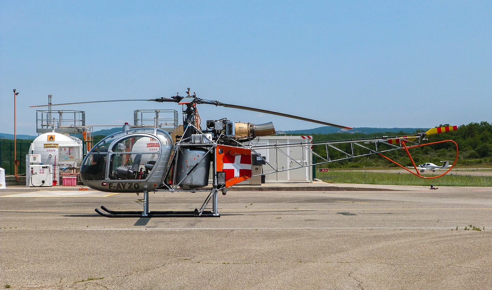 Silberner Hubschrauber Alouette II mit Gitterrohrheck und offen liegender Turbine auf einem Flugplatzvorfeld