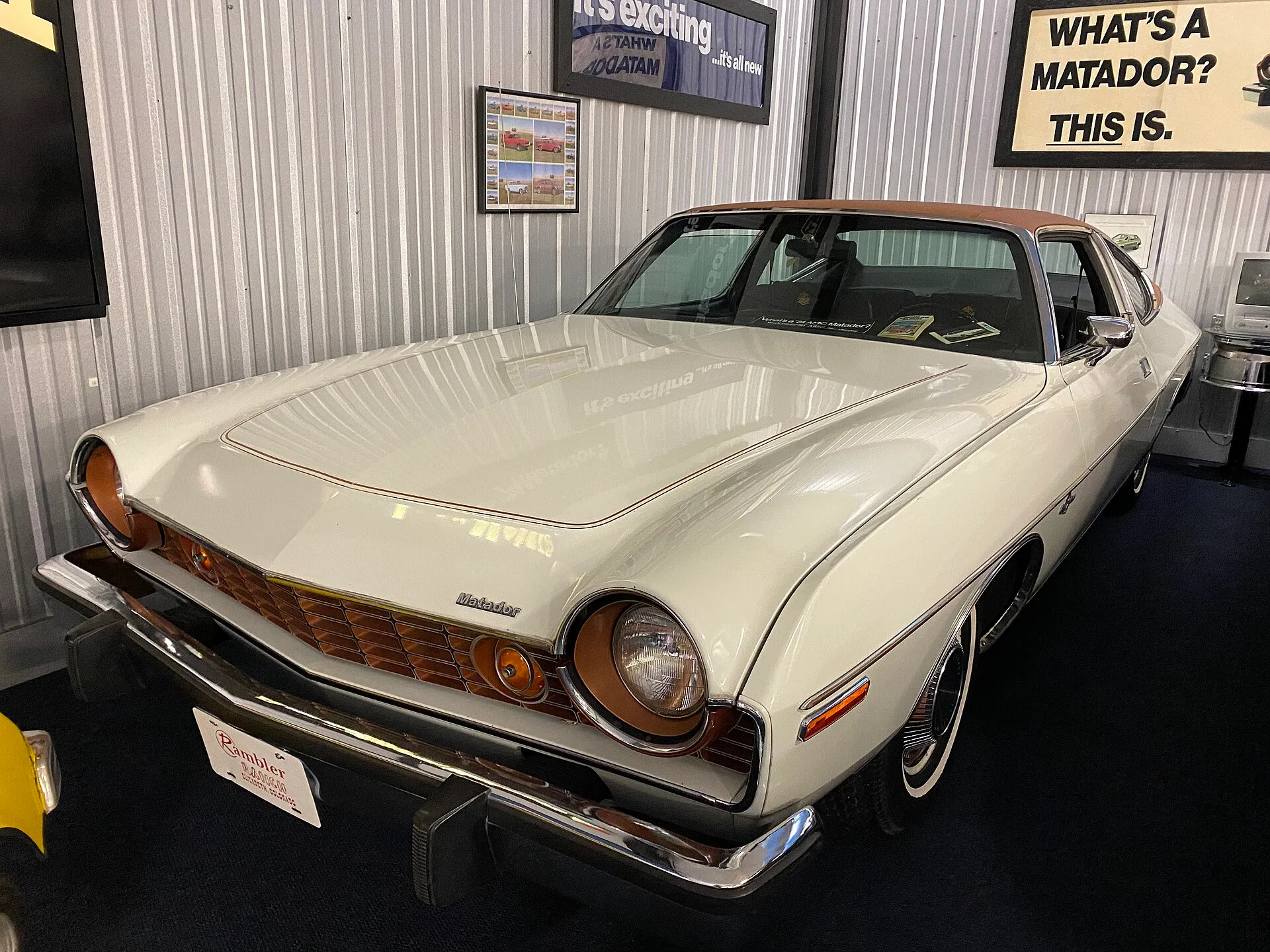 Weißes AMC-Matador-Coupé von 1974 mit kupferfarbenem Dach und den tief eingelassenen Scheinwerferfassungen in einer Sammlungshalle