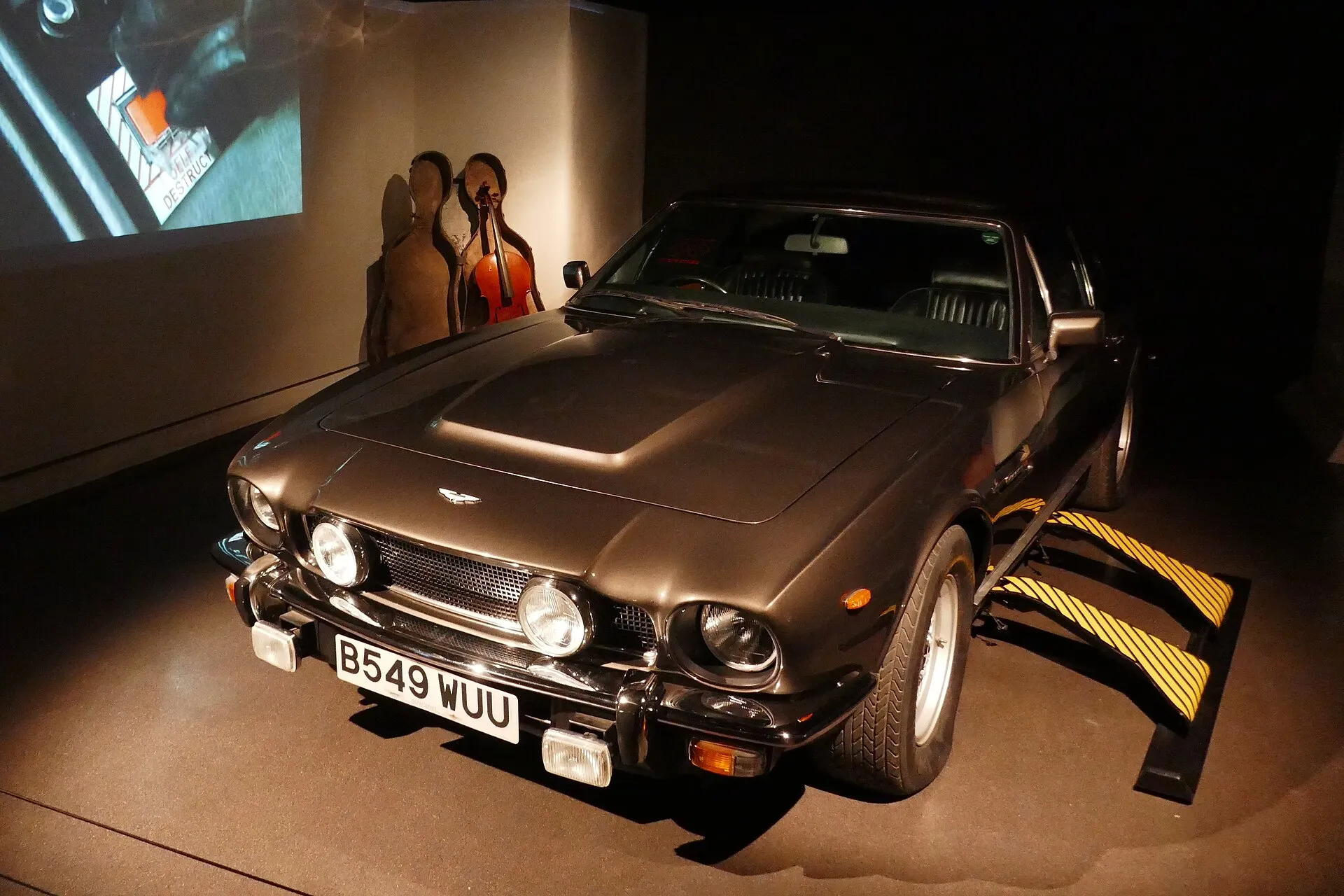 Aston Martin V8 und Cellokoffer-Schlitten aus dem Film in einer Ausstellung