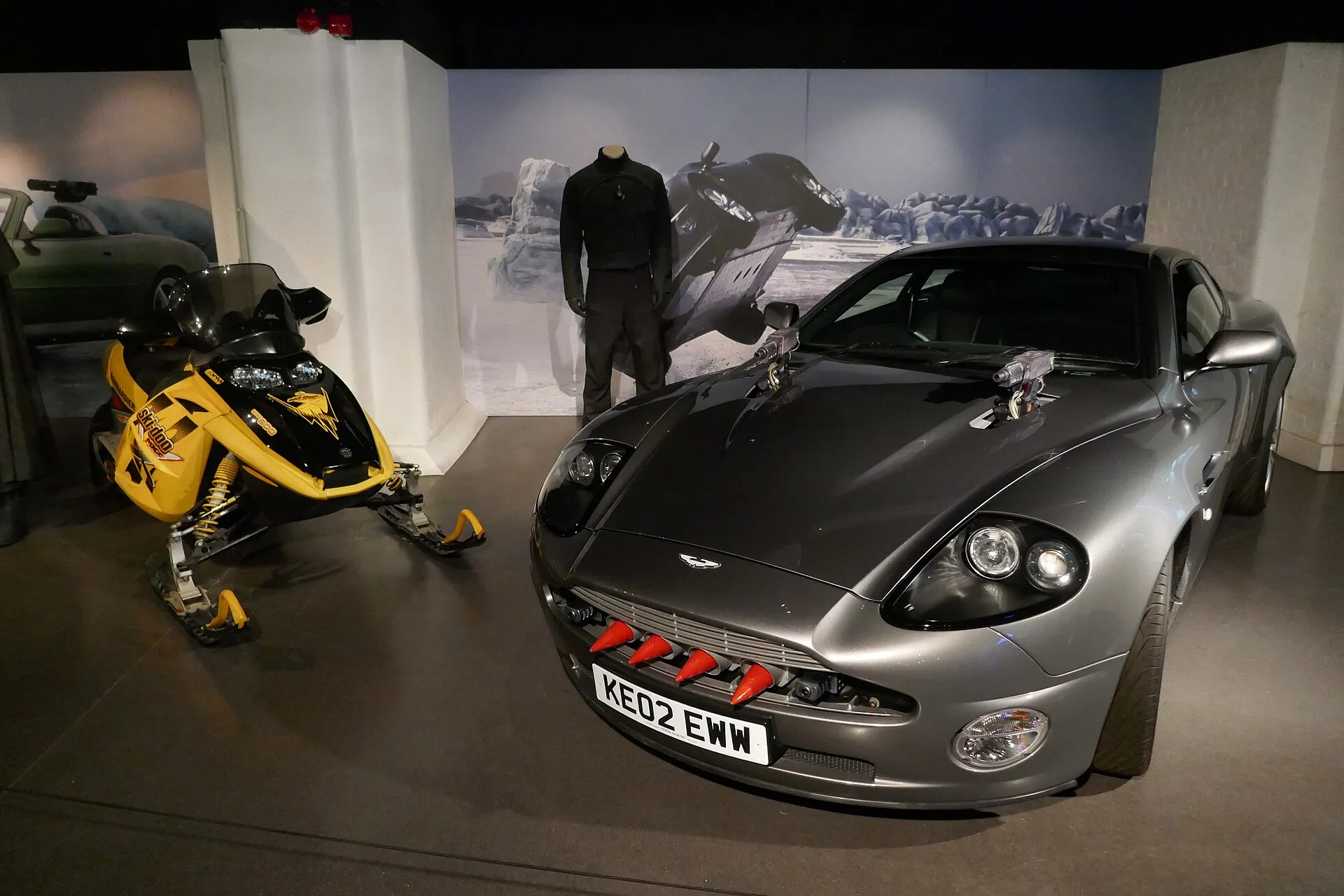 Bewaffneter silberner Aston Martin V12 Vanquish neben einem gelben Ski-Doo aus dem Film
