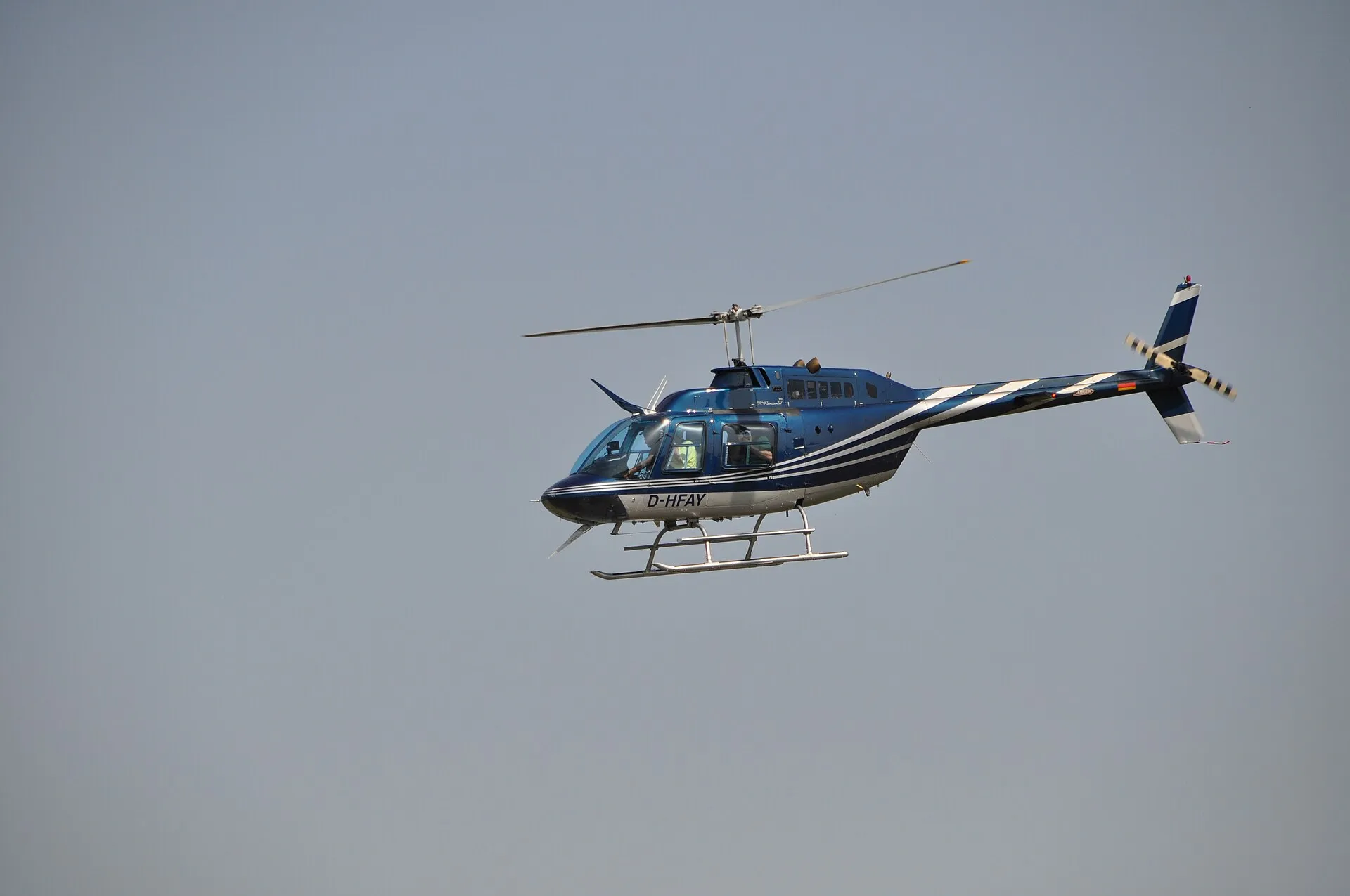 Blau-weißer Hubschrauber Bell 206 JetRanger mit der Kennung D-HFAY im Flug vor grauem Himmel