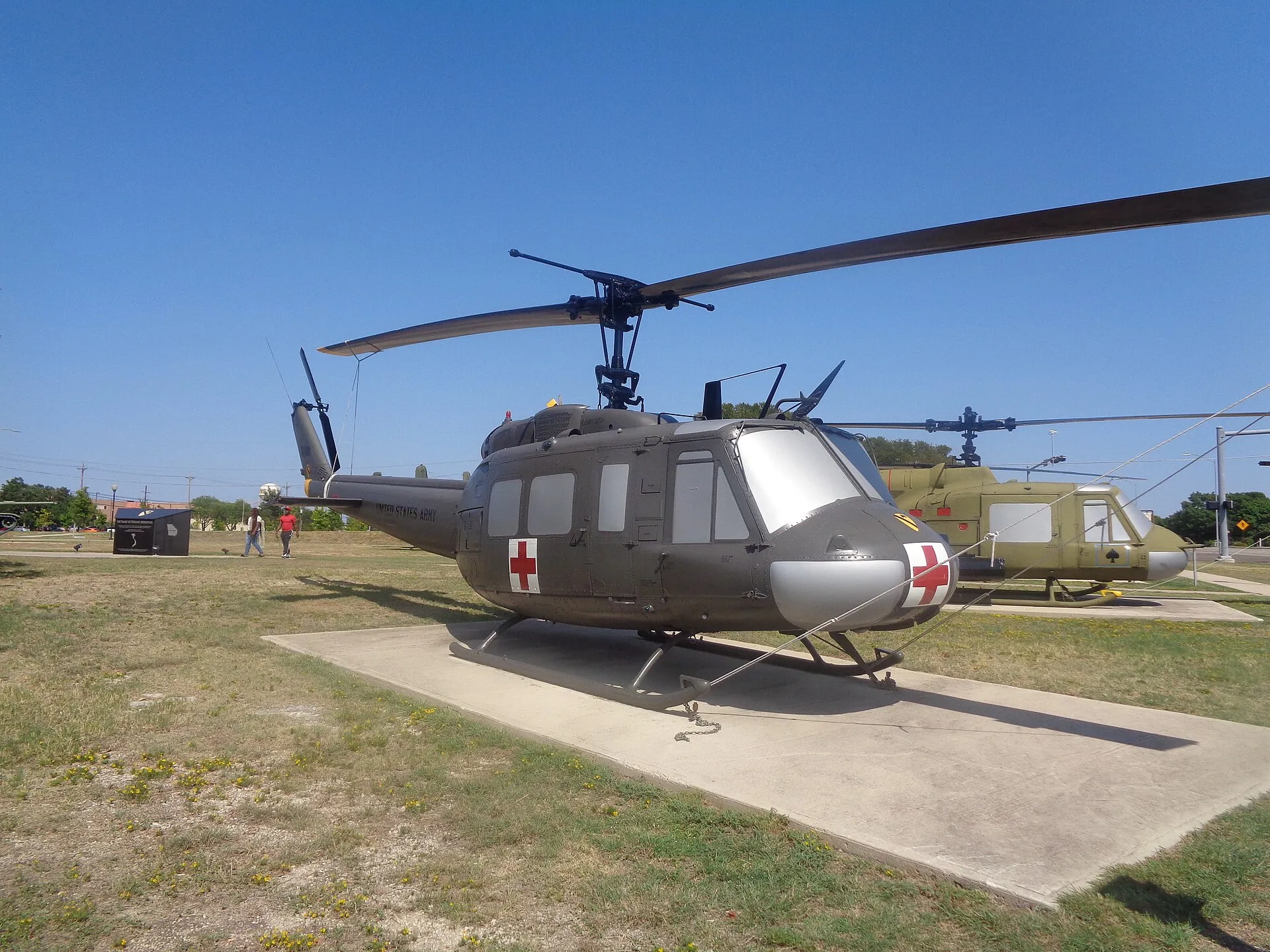 Olivgrüner Bell UH-1H mit Rotkreuzmarkierungen vor einem Militärmuseum.
