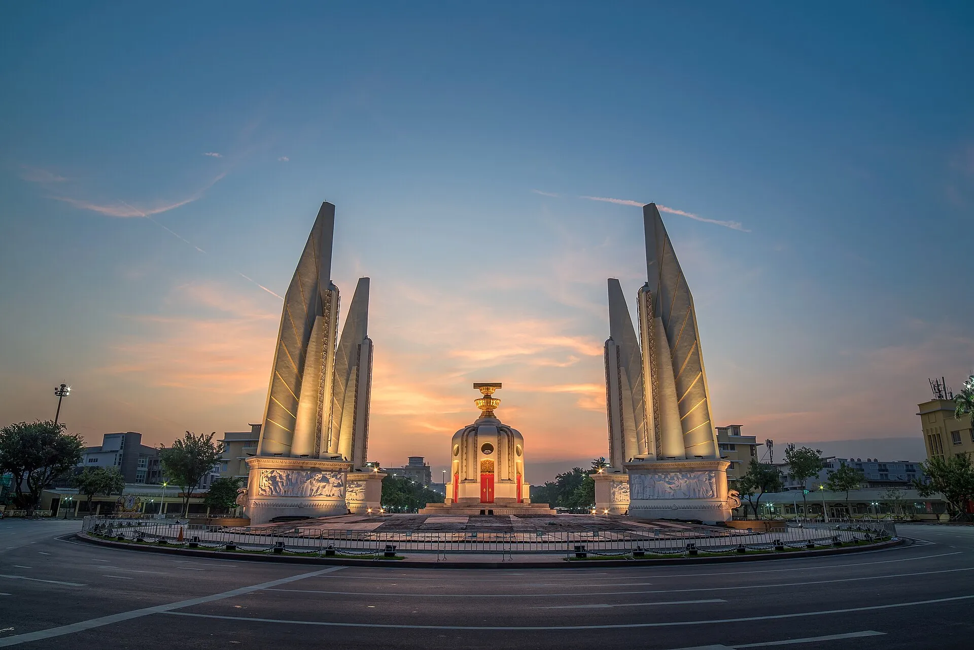 Das Democracy Monument mit seinen vier flügelartigen Pfeilern und dem beleuchteten Mittelbau im Kreisverkehr der Ratchadamnoen-Avenue in Bangkok, aufgenommen in der Abenddämmerung