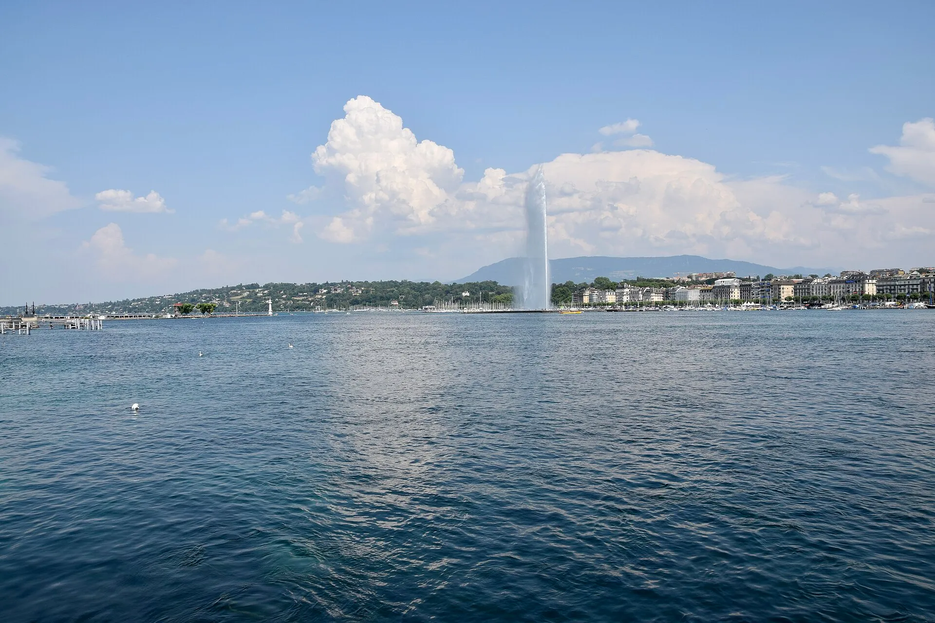 Der Jet d'Eau auf dem Genfersee vor der Uferpromenade und den Häuserzeilen von Genf