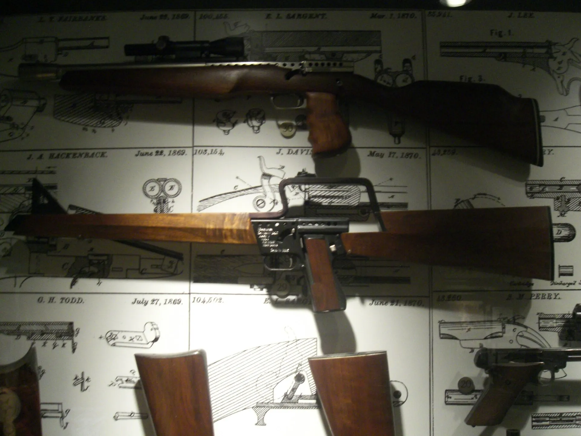 Gyrojet-Karabiner und -Gewehr mit Holzschaft an einer Museumswand vor Patentzeichnungen
