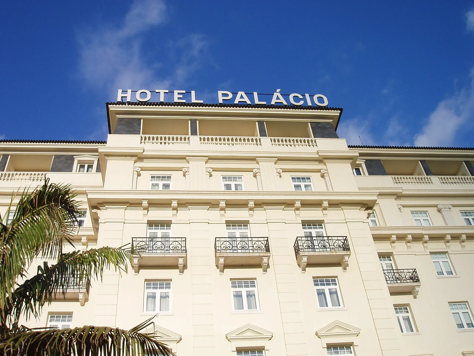 Helle Fassade des Hotel Palácio in Estoril mit Balkonen und dem Schriftzug „Hotel Palácio“ auf dem Dach