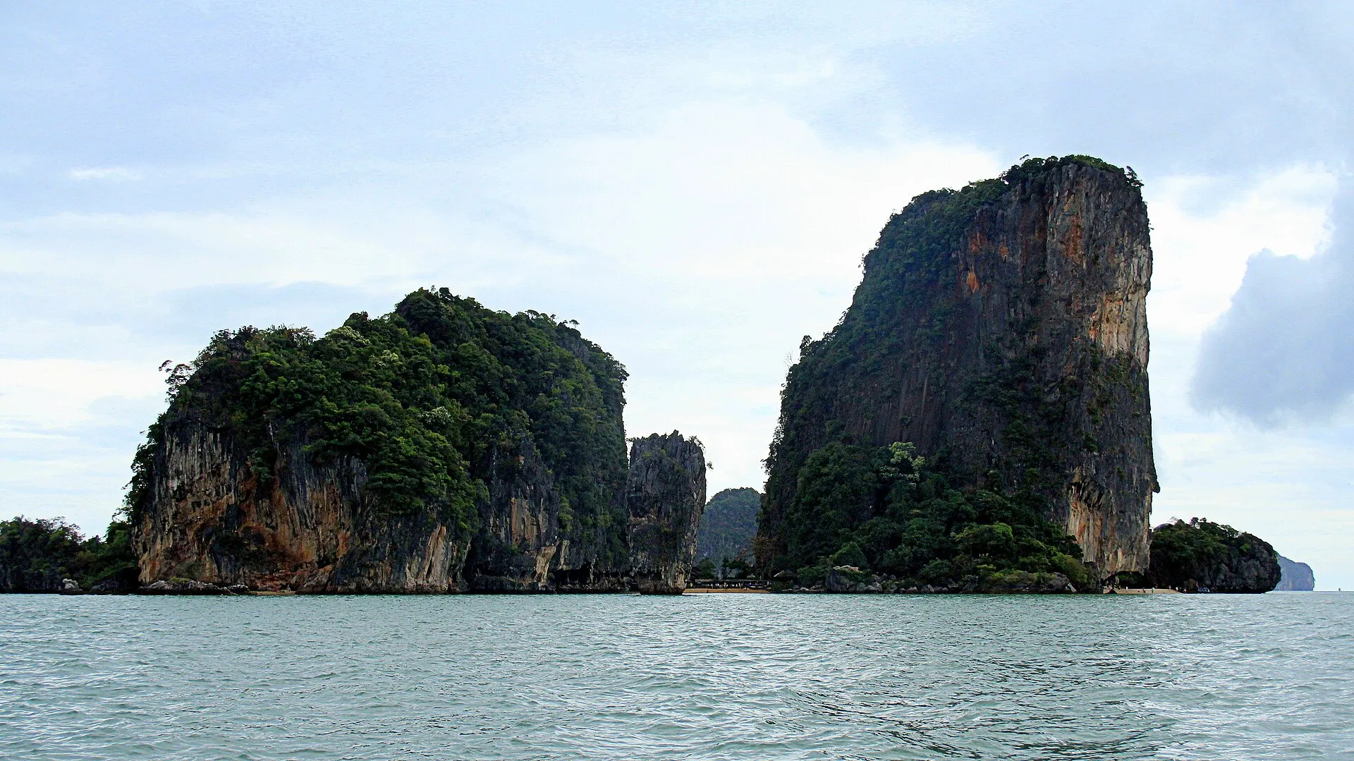 Die beiden bewaldeten Kalksteinfelsen von Khao Phing Kan über dem Meer der Phang-Nga-Bucht, dazwischen der schmale Strand mit der Felsnadel Ko Tapu