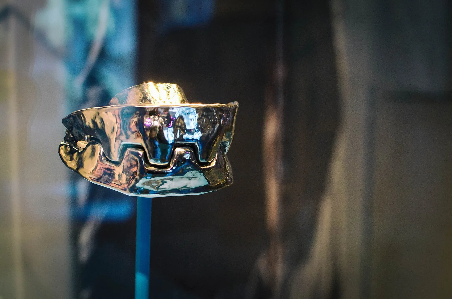 Ein poliertes Metallgebiss mit stumpfen, zahnradartigen Zähnen auf einem Ständer in einer dunklen Vitrine