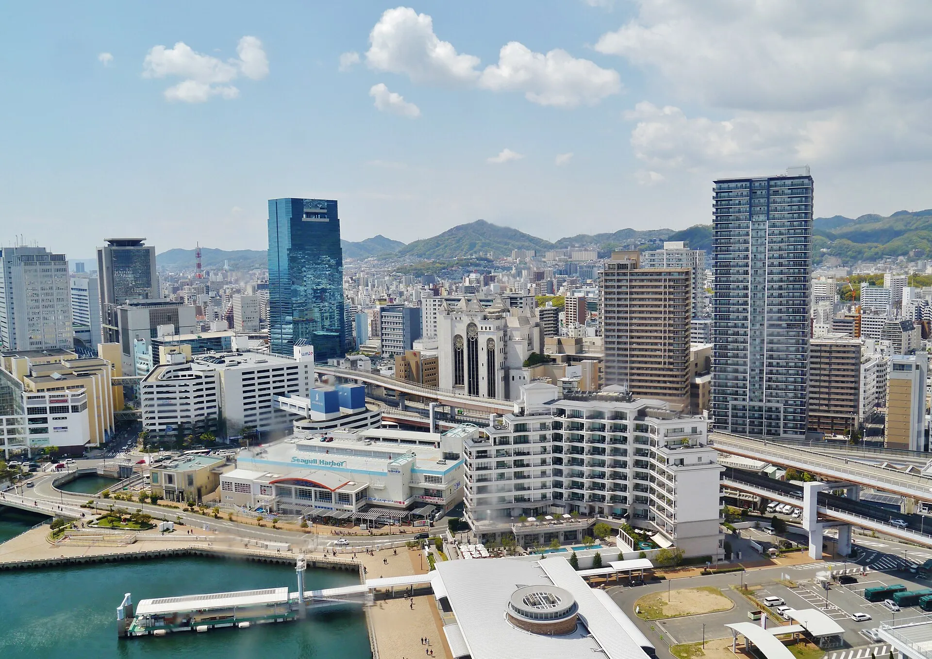 Blick vom Kobe Port Tower über Hafenbecken, Kais und die Stadt vor bewaldeten Bergen