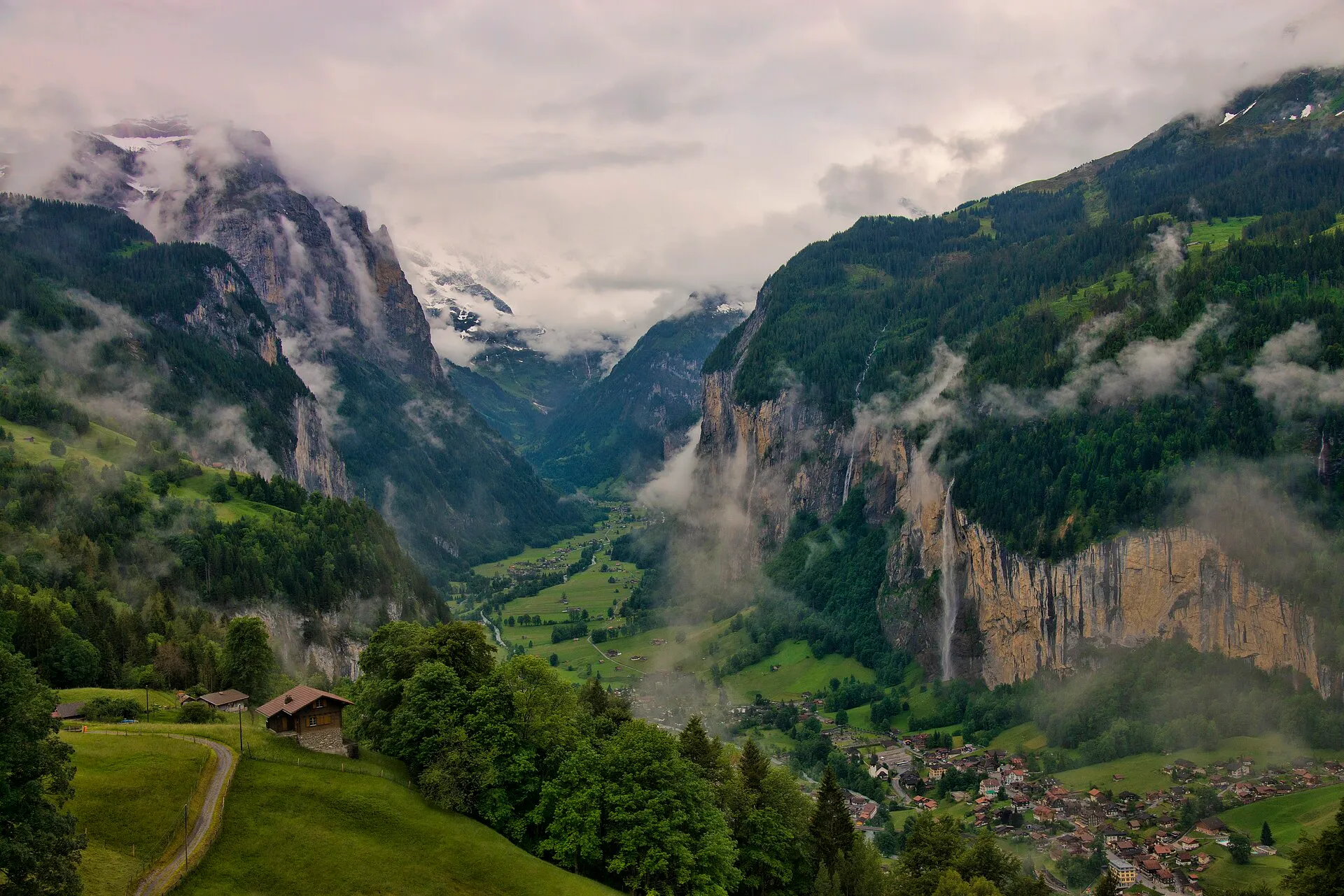 Blick über das Lauterbrunnental mit Wolkenfetzen, Wasserfällen an den Felswänden und dem Dorf am Talboden