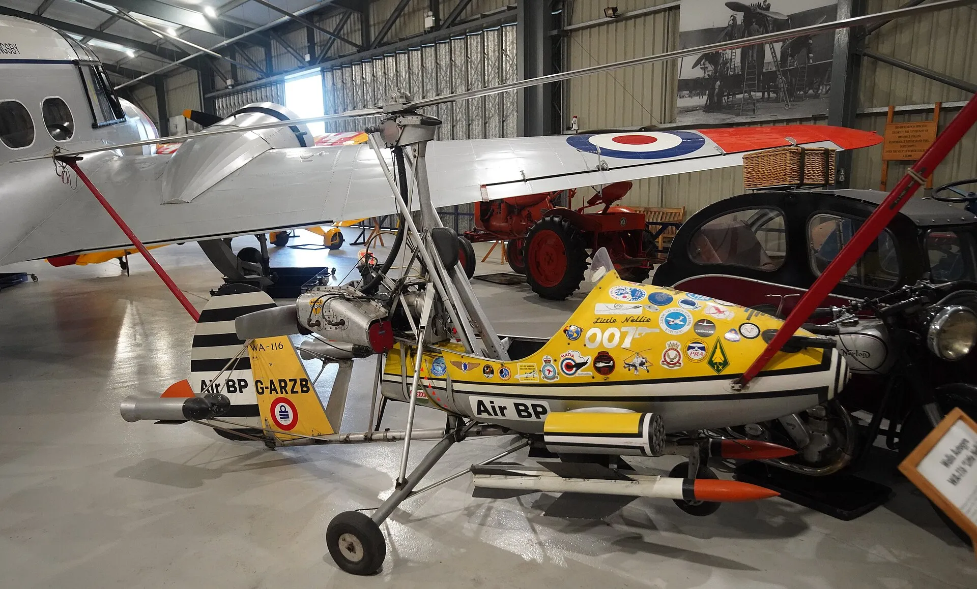 Der gelbe Tragschrauber „Little Nellie“ mit der Kennung G-ARZB, Raketenattrappen und 007-Aufschrift in einem Hangar