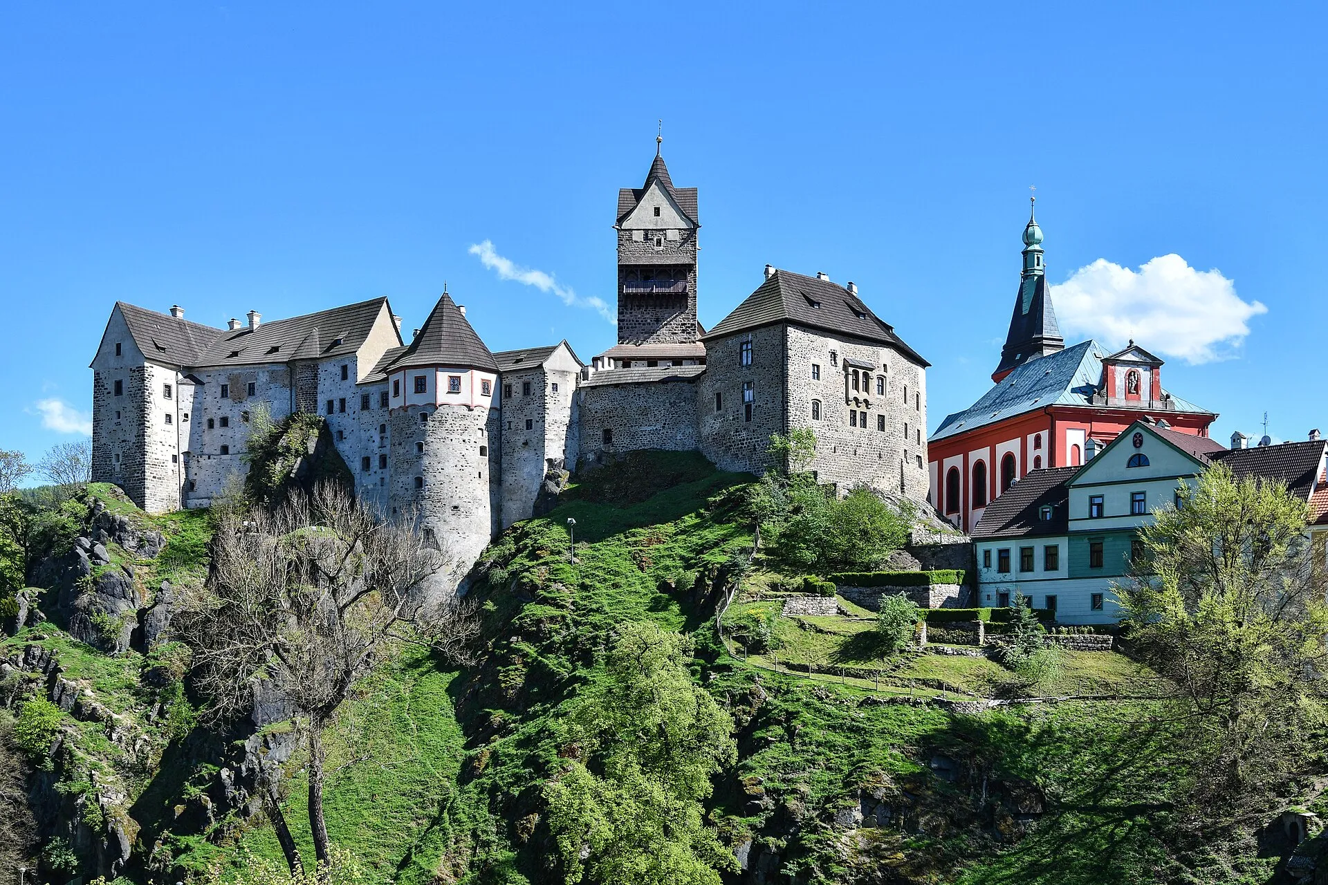 Burg Loket über bewaldeten Felsen unter blauem Himmel