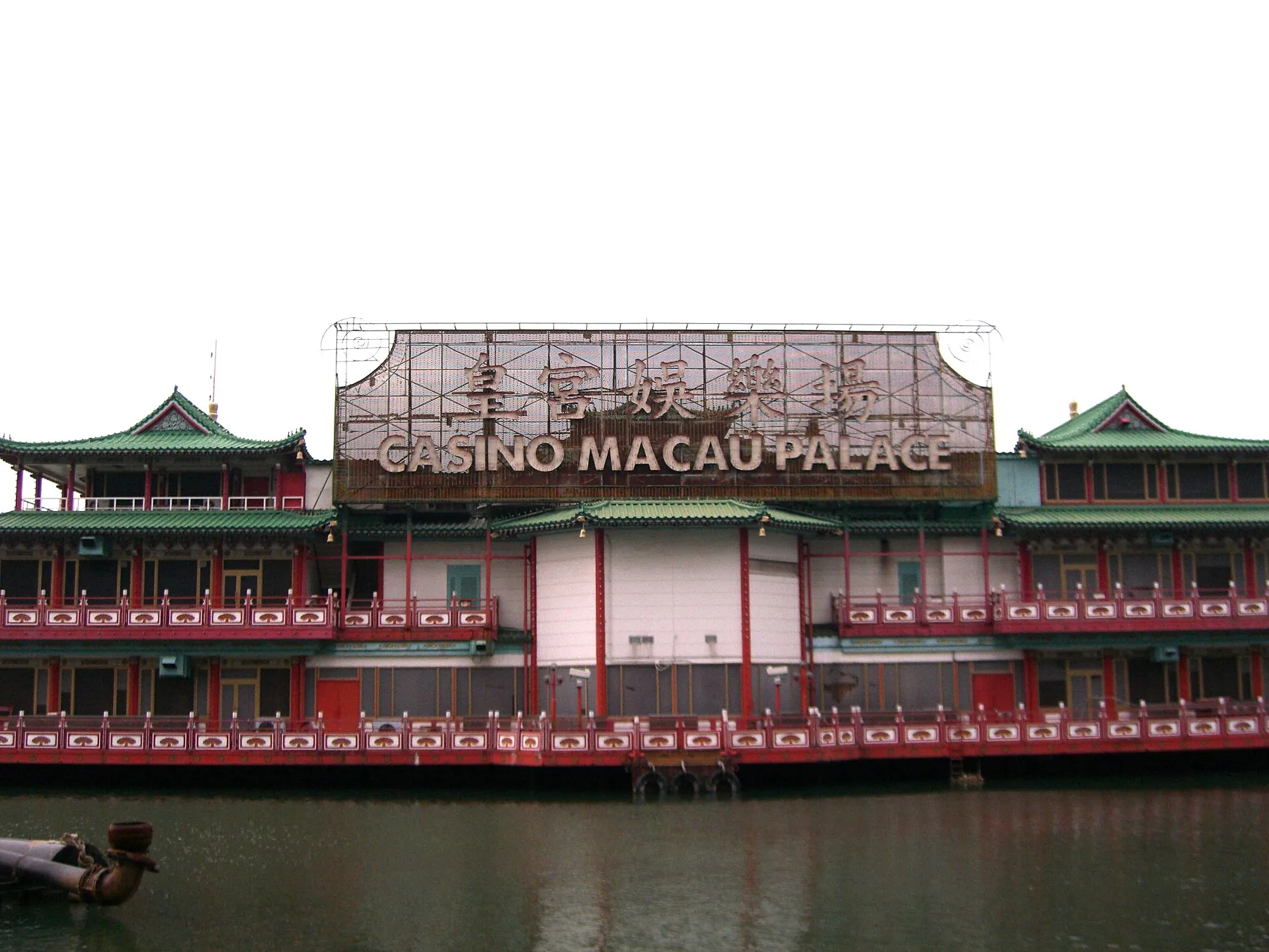 Das schwimmende Kasino Macau Palace, ein dreistöckiger Schiffsbau mit roten Balustraden, grünen Pagodendächern und dem Schriftzug „Casino Macau Palace“