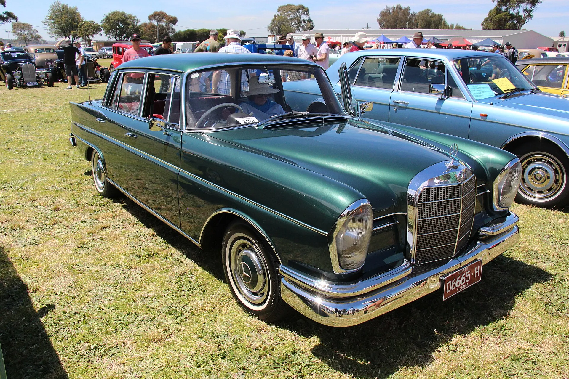 Dunkelgrüne Mercedes-Benz-Heckflossen-Limousine der Baureihe W111 auf einer Wiese bei einem Oldtimertreffen