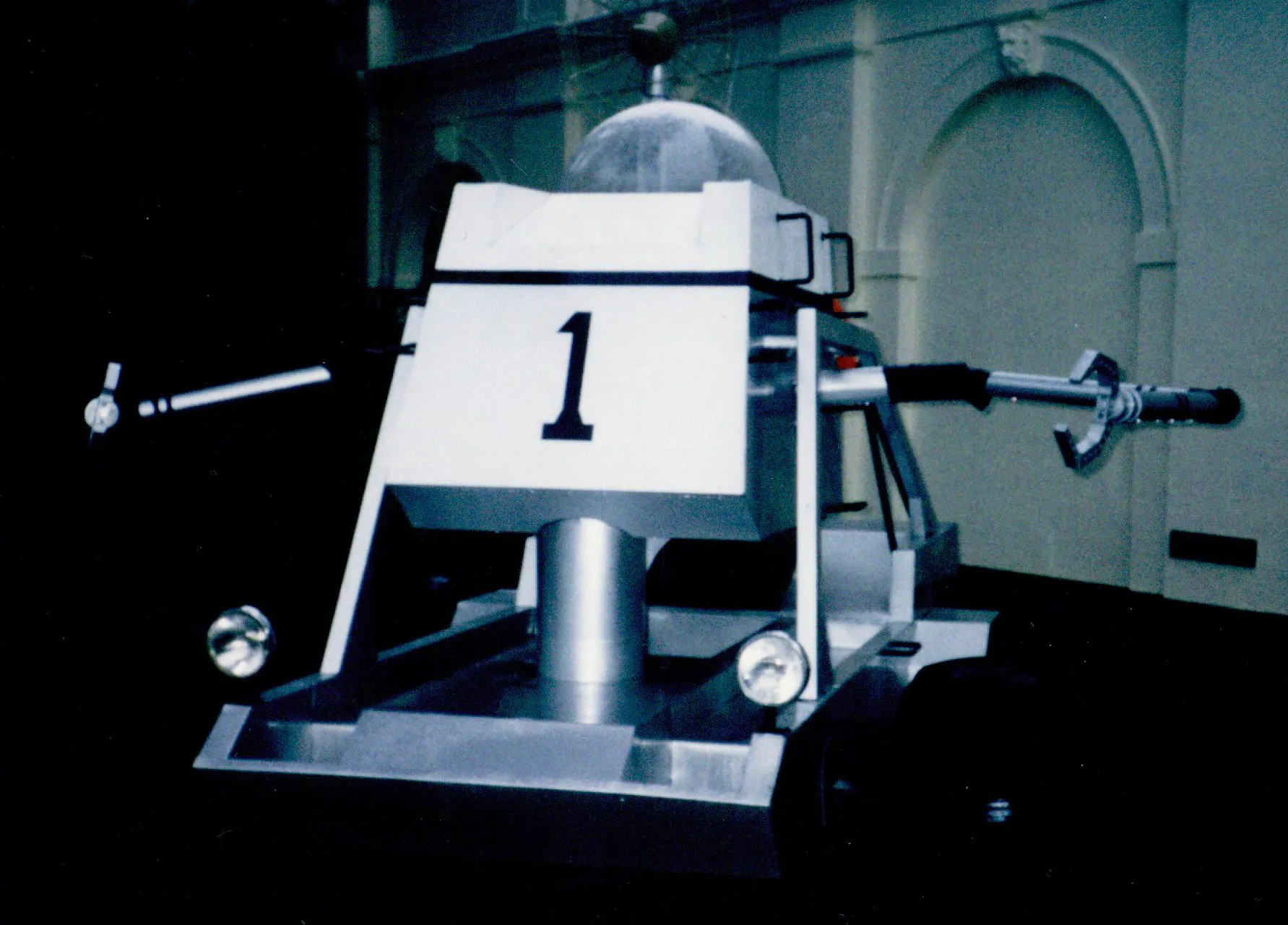 Weißer Mondbuggy mit Plexiglaskuppel und seitlich ausgestreckten Greifarmen in einer Ausstellung.