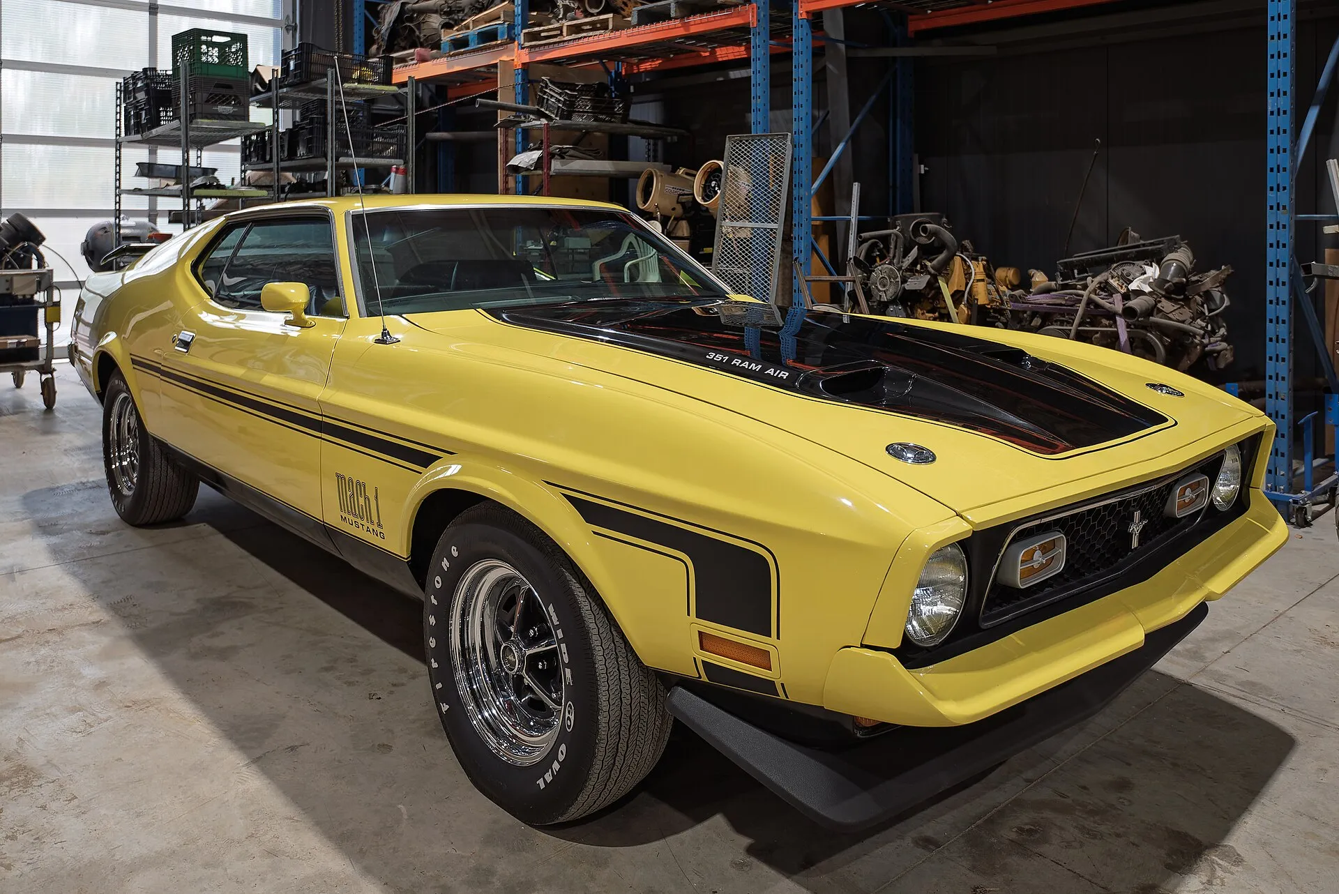 Gelber Ford Mustang Mach 1 von 1971 mit schwarzer Motorhaube in einer Halle.