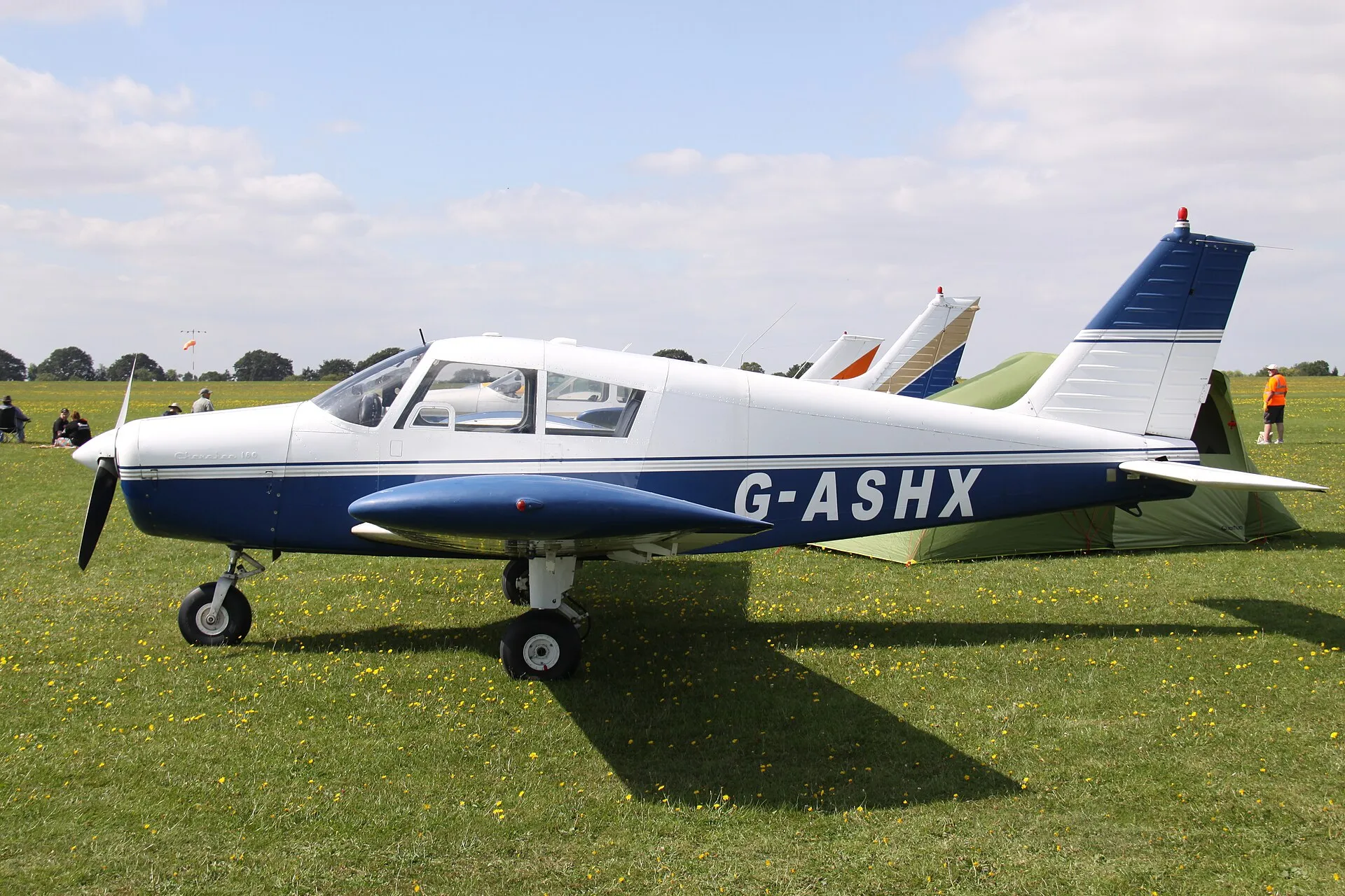 Blau-weiße Piper PA-28-180 Cherokee B mit der Kennung G-ASHX auf einem Grasflugplatz