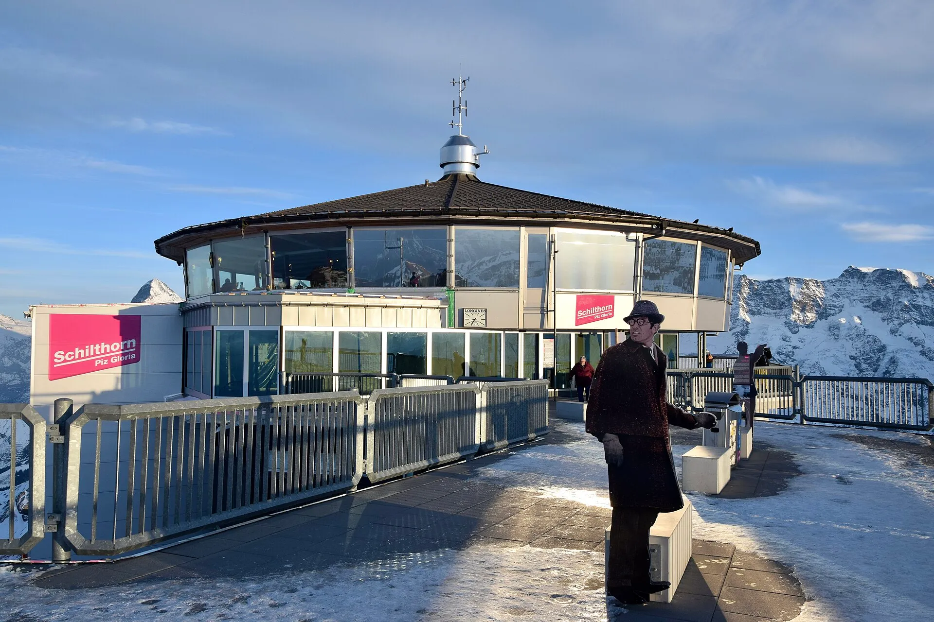 Das runde Gipfelgebäude des Schilthorns mit der Aufschrift „Schilthorn Piz Gloria“ und einer Bond-Figur aus Pappe auf der verschneiten Terrasse