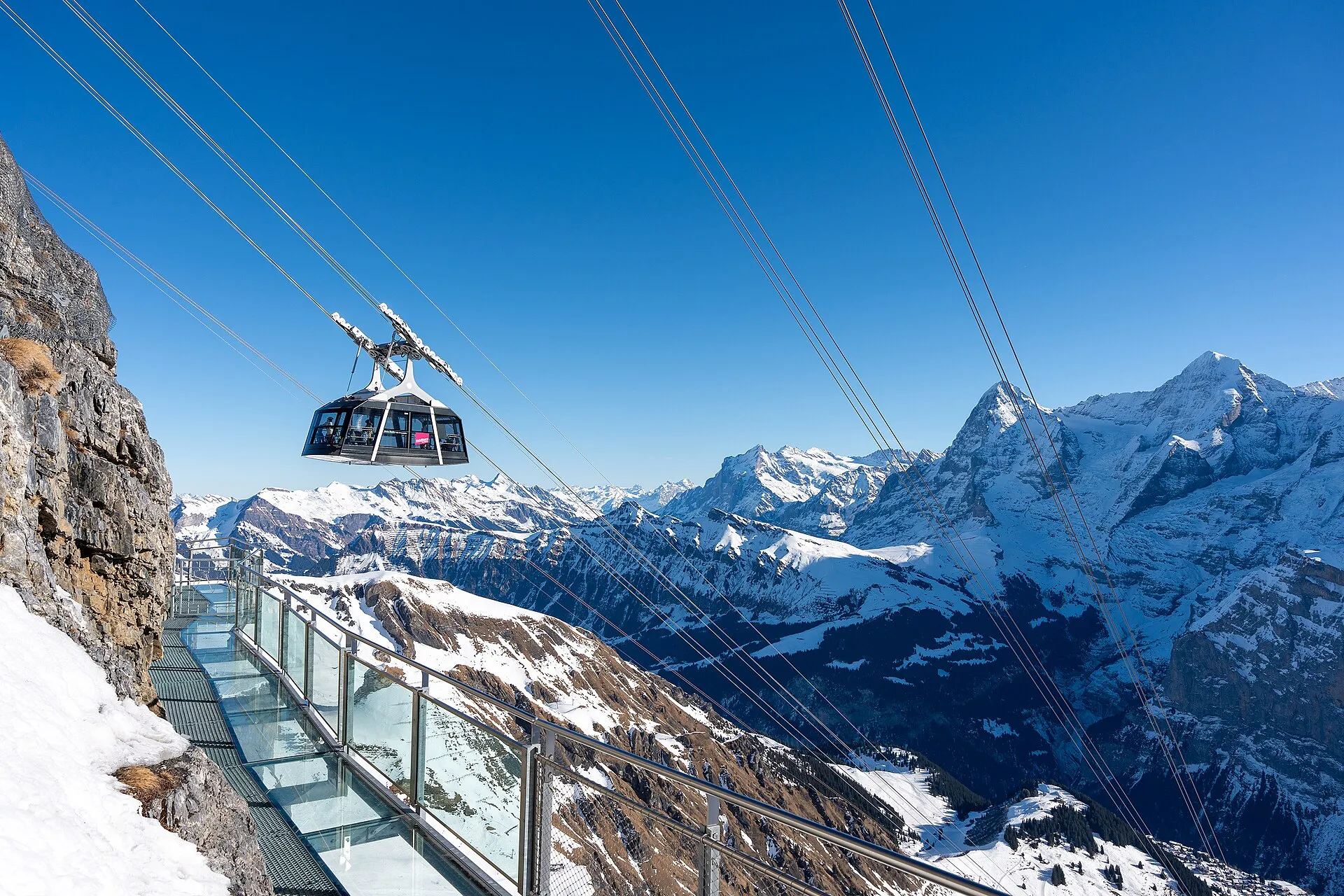 Kabine der Schilthornbahn über einem Felsgrat, dahinter die verschneiten Gipfel von Eiger, Mönch und Jungfrau