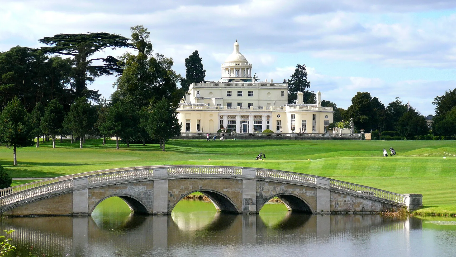 Das Herrenhaus von Stoke Park hinter der Repton-Bogenbrücke über den See, davor der Golfplatz