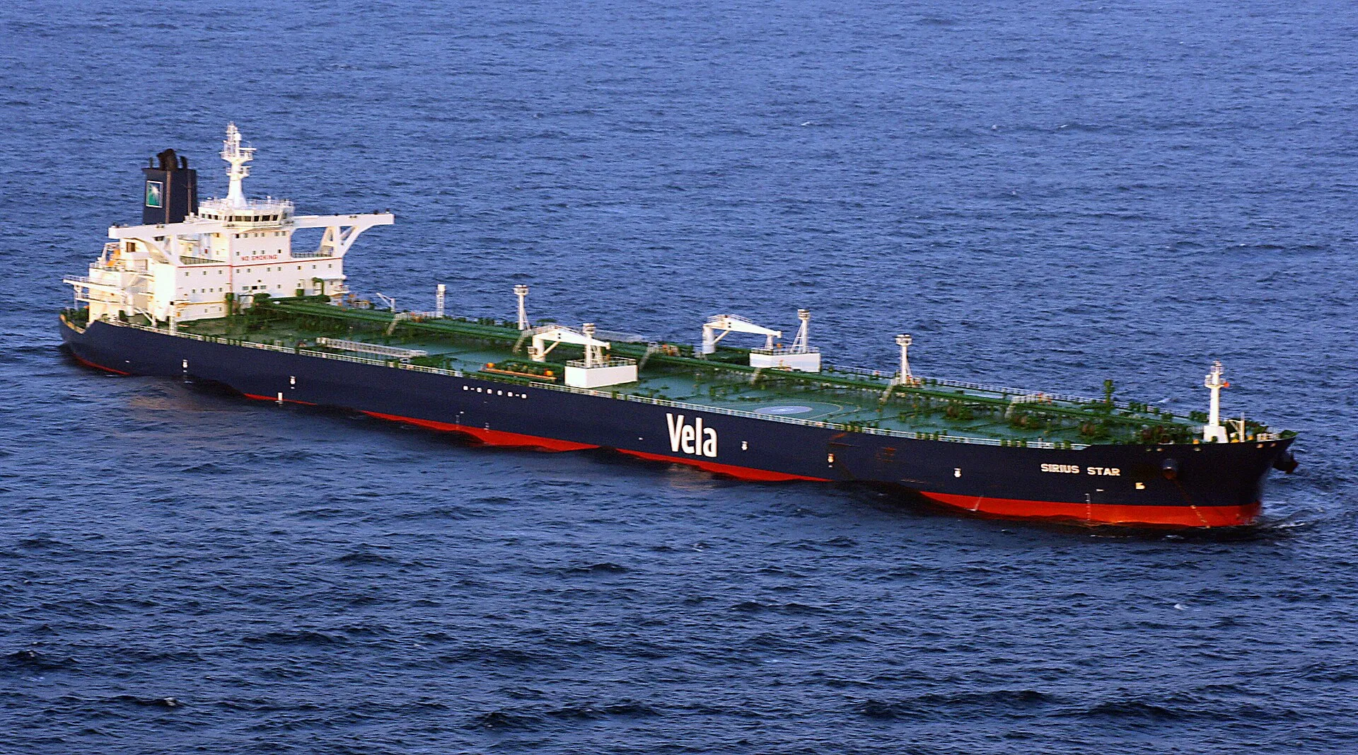 Luftaufnahme eines voll beladenen Supertankers mit dunklem Rumpf, grünem Deck und achterem Aufbau auf offener See