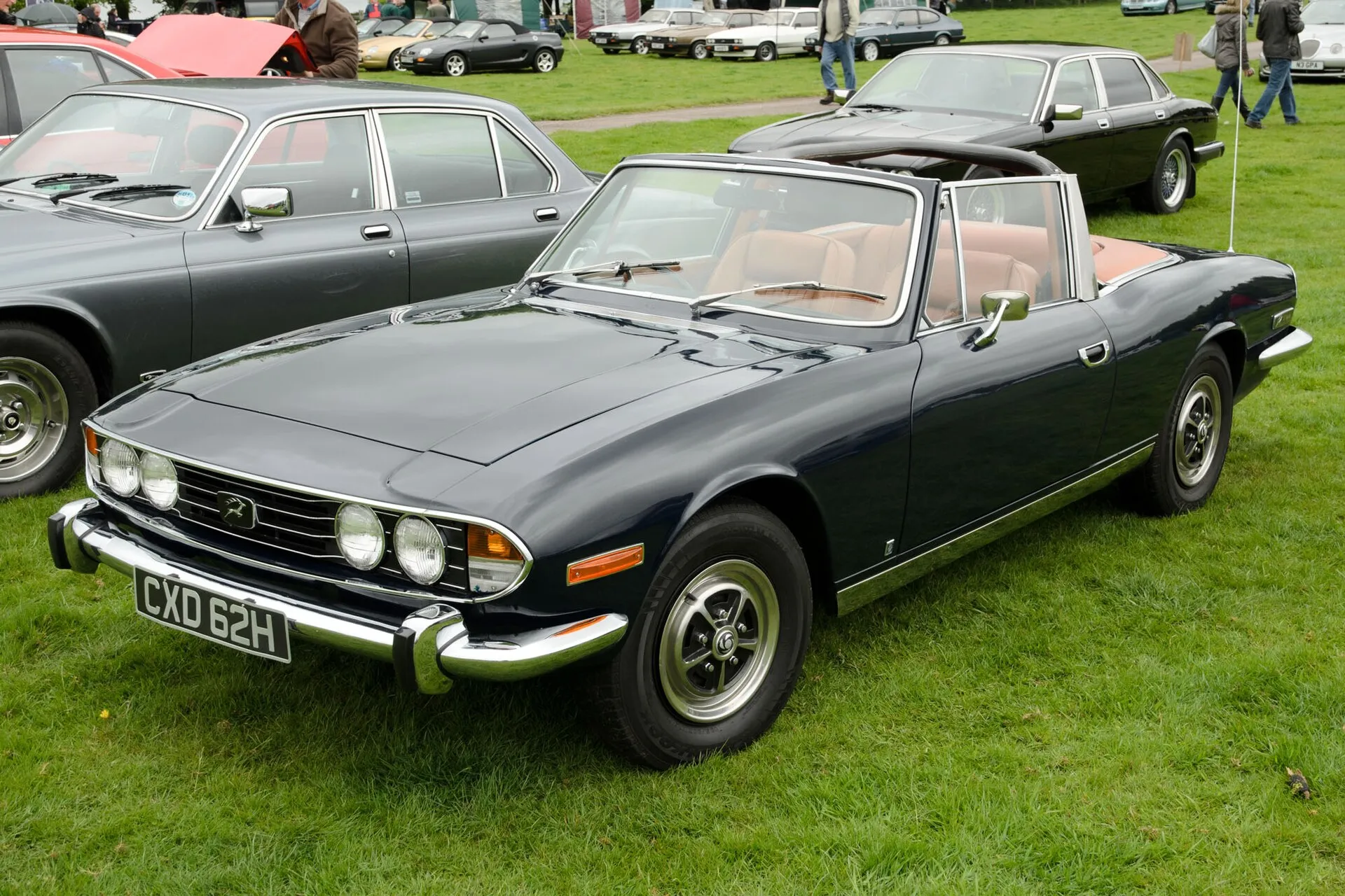 Dunkler Triumph Stag mit geöffnetem Verdeck bei einem Oldtimertreffen.